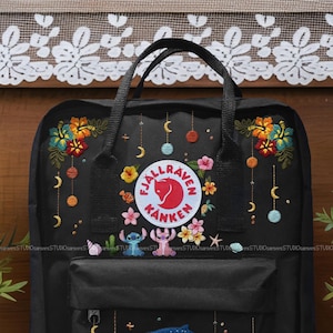 Può includere: Zaino nero con ricami floreali e celesti. Presenta un logo circolare con una volpe rossa. Include i personaggi ricamati di Stitch e Angel e una conchiglia. Lo zaino ha un manico superiore e spallacci regolabili.