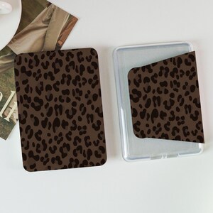 May include: Brown leopard print phone case and card holder. The case is clear with a brown leopard print insert. The card holder is a matching brown leopard print. The items are on a white surface.