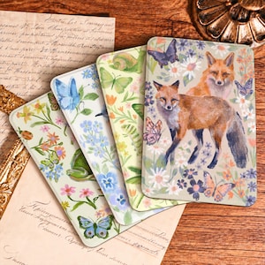 May include: Four rectangular coasters featuring detailed illustrations of nature. The designs include foxes, butterflies, a frog, a ladybug, a snail, a caterpillar, and various colorful flowers, all set against light-colored backgrounds.