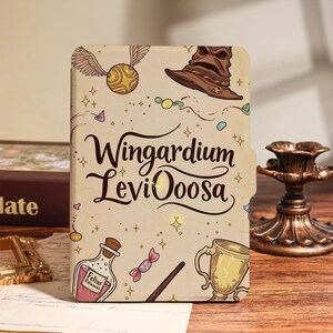 Peut inclure: Une couverture de cahier beige avec des illustrations d'un vif d'or, d'un chapeau de sorcier, d'une bouteille de potion, d'une baguette et d'un trophée. Les mots "Wingardium Leviooosa" sont écrits dans une police stylisée. La couverture a un onglet sur le côté droit.