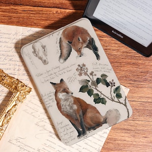 Op de afbeelding: Een beige Kindle-hoes met een gedetailleerde illustratie van een vos, botanische elementen en handgeschreven notities. De hoes heeft bruine en groene accenten en bevat een schedel en een vosillustratie.