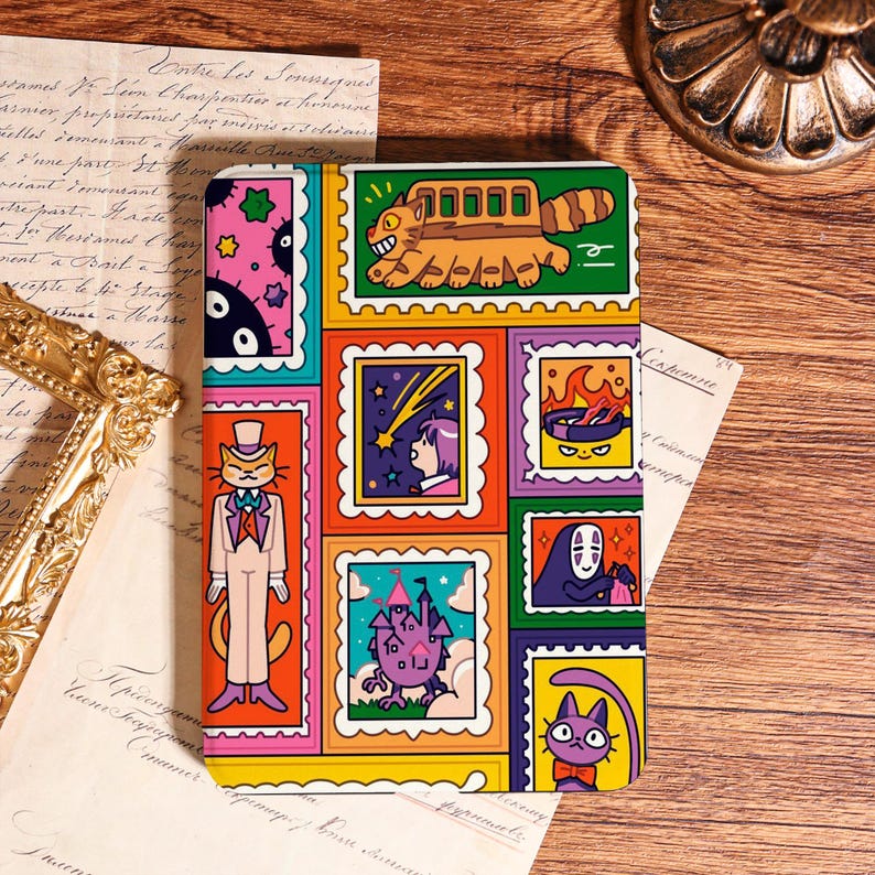 May include: A colorful notebook featuring a collage of cartoon illustrations in a postage stamp design. The images include a cat in a suit, a bus-like creature, a girl watching a shooting star, and a purple cat with a bow tie. The notebook is on a wooden surface.