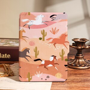 May include: A tablet case featuring a desert landscape with running horses and cacti. The case has a pink and peach background with illustrations of horses in various colors, including white, brown, and gray. The design includes green cacti and desert plants.