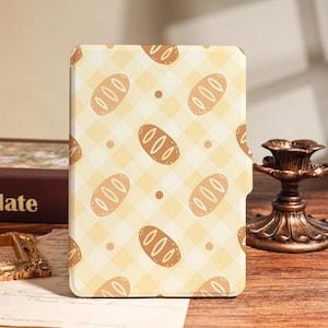 May include: A rectangular e-reader case featuring a repeating pattern of light brown bread loaves and small dots set against a pale yellow and cream-colored checkered background. The case has a smooth, flat surface with a notched edge on the right side.