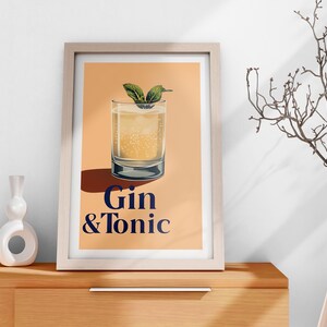 May include: A framed print with a peach background featuring a glass of gin and tonic with a sprig of mint. The text "Gin & Tonic" is printed in blue below the glass.