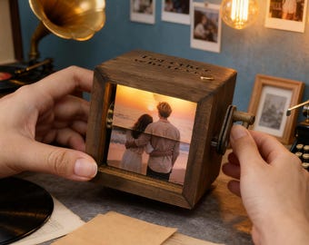 May include: A wooden photo cube with a crank, displaying a sunset image of a couple. The cube has the words "Together wherever" engraved on it. The cube is held by hands, with a vintage gramophone and typewriter in the background.