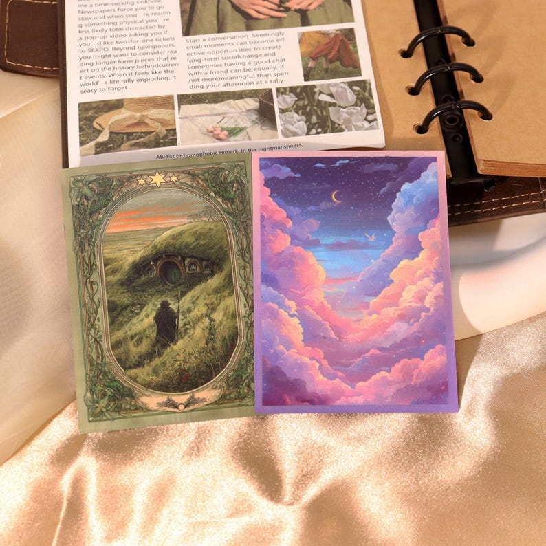 May include: Two rectangular stickers featuring artistic illustrations. The left sticker shows a figure standing before a round door in a grassy hill within an ornate green frame. The right sticker depicts a vibrant night sky with pink and blue clouds.