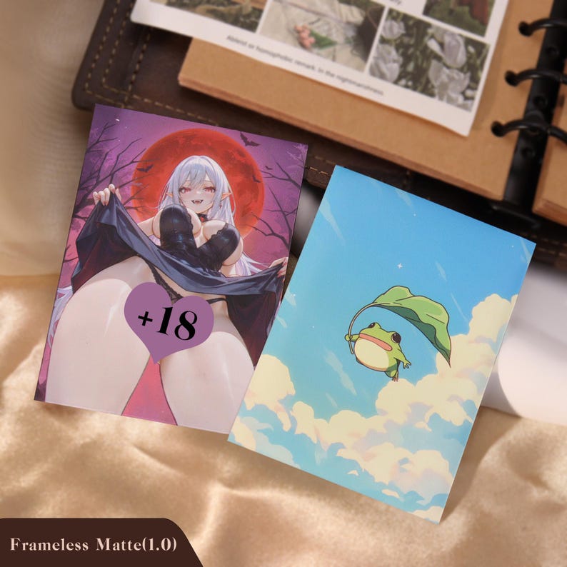 May include: Two rectangular art prints. One print features an anime-style character with white hair and fangs against a red moon background with a purple heart overlay containing the text +18. The second print shows a green frog holding a leaf in the sky.
