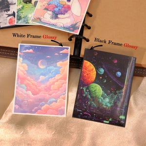May include: Two rectangular glossy prints featuring distinct illustrations. The left print displays a pastel sky with pink and blue clouds and a crescent moon. The right print shows a dark space scene with vibrant planets and a futuristic city.