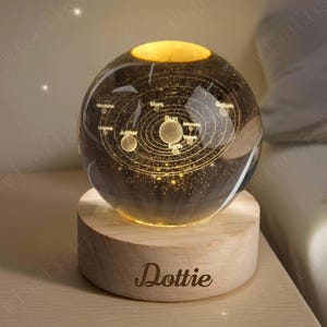 May include: A lit glass sphere showing a solar system model, set on a wooden base. The sphere has illuminated planets and orbits, with the sun at the centre. The wooden base is engraved with the name "Dottie".