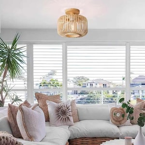 Può includere: Un divano bianco con cuscini in un soggiorno con un lampadario in legno intrecciato. Il divano è davanti a una finestra con tende bianche.