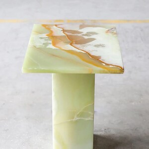 May include: A square, green onyx side table with a rectangular base. The tabletop features a mix of green, white, and gold veining. The table is approximately 24 inches tall.
