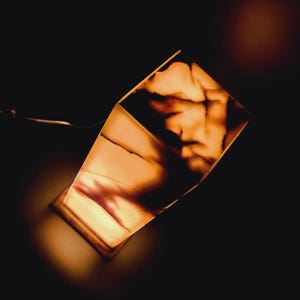 Puede incluir: Una l&aacute;mpara geom&eacute;trica transl&uacute;cida hecha de &oacute;nix con un c&aacute;lido resplandor naranja. La l&aacute;mpara est&aacute; encendida y la luz brilla a trav&eacute;s de la piedra, creando un hermoso patr&oacute;n.