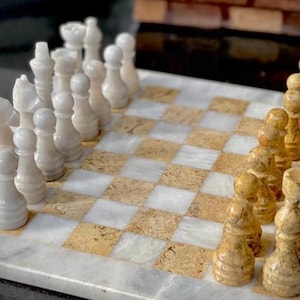 May include: A marble chess set with white and beige pieces on a white and beige marble chessboard.