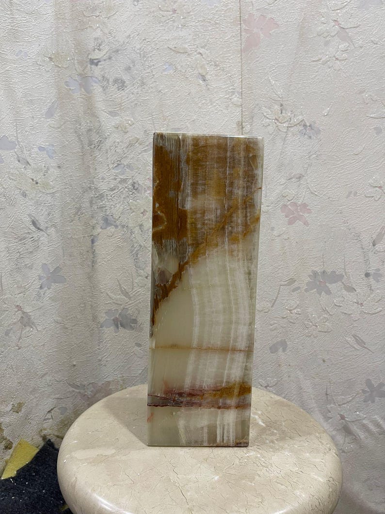 Puede incluir: Un jarr&oacute;n alto y rectangular hecho de &oacute;nix blanco y marr&oacute;n con un patr&oacute;n natural estriado. El jarr&oacute;n tiene un acabado liso y pulido.