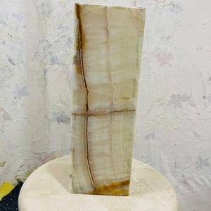 Puede incluir: Un jarr&oacute;n alto y rectangular hecho de &oacute;nix blanco y marr&oacute;n. El jarr&oacute;n tiene una superficie lisa y pulida y un patr&oacute;n natural y org&aacute;nico.