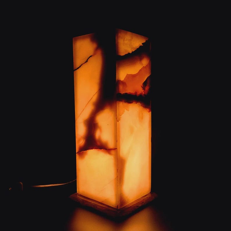 Puede incluir: Una l&aacute;mpara rectangular de &oacute;nix con un c&aacute;lido brillo naranja. La l&aacute;mpara tiene un patr&oacute;n natural de m&aacute;rmol con vetas marrones y blancas.
