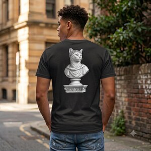 Könnte beinhalten: Ein schwarzes Kurzarm-T-Shirt mit einem weißen Grafikdruck auf der Rückseite. Das Design zeigt eine klassische Steinbüste einer Katze mit Lorbeerkranz, die auf einem dekorativen Sockel steht und in Grau- und Weißtönen dargestellt ist.