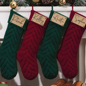 Może przedstawiać: Cztery spersonalizowane skarpety świąteczne w kolorze zielonym i czerwonym, z tkanym wzorem w jodełkę. Każda skarpeta ma skórzaną metkę z imieniem: Patrick, Kelley, Austin i Sophia. Świąteczna dekoracja.