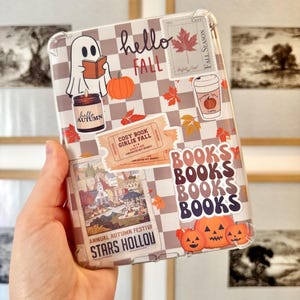 Op de afbeelding: Transparante telefoonhoes met een herfstthema. De hoes heeft een geruit patroon en stickers met pompoenen, bladeren, een lezende geest en de woorden "hello FALL", "BOOKS" en "STARS HOLLOW".