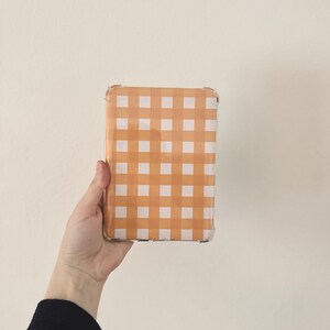 Puede incluir: Una funda transparente para teléfono con un patrón de cuadros vichy en naranja y blanco.