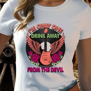 May include: White t-shirt featuring a graphic design with a guitar, wings, and roses. The text reads "I'm Only One Drink Away From The Devil". The guitar is coral, the wings are salmon, and the roses are magenta.