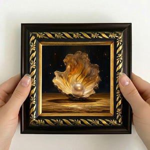 Op de afbeelding: Een ingelijst schilderij van een parel in een schelp. Het kunstwerk toont een donkere achtergrond met een gouden schelp en een parel. De lijst is donkerbruin met gouden accenten. Het schilderij wordt door twee handen vastgehouden.