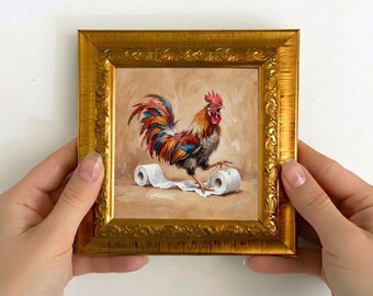 May include: A square painting in an ornate gold frame depicting a colorful rooster with red, blue, and brown feathers standing on a trail of white toilet paper against a light brown background. The rooster has its beak open as if crowing.