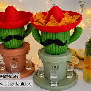Könnte beinhalten: Zwei kaktusförmige Serviersets mit roten Sombrero-Schalen, gefüllt mit Tortilla-Chips. Jeder grüne Kaktus hat einen schwarzen Schnurrbart und steht auf einem Sockel mit drei klaren Schnapsgläsern. Der Text auf dem Bild lautet: Shotverteiler Mr. Nacho Kaktus.