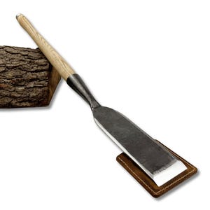 May include: A woodworking chisel with a light wood handle and a dark metal blade. The blade rests on a small, brown leather sheath. The chisel is angled towards the viewer, suggesting its use in carving or shaping wood.