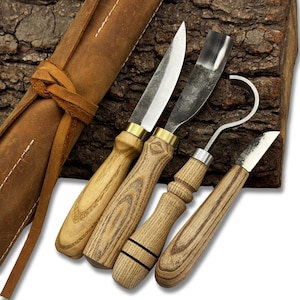 Puede incluir: Un juego de cuatro herramientas para tallar madera con mangos de madera y hojas de metal. Las herramientas incluyen un cuchillo recto, una gubia curva, un cuchillo de gancho y un cuchillo sesgado. Un estuche de herramientas de cuero marrón está en el fondo.