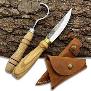 Puede incluir: Un juego de herramientas para tallar madera, que incluye un cuchillo de gancho, un cuchillo de hoja recta y una funda de cuero. Los cuchillos tienen mangos de madera y hojas de metal. La funda es de cuero marrón con cierre de botón.