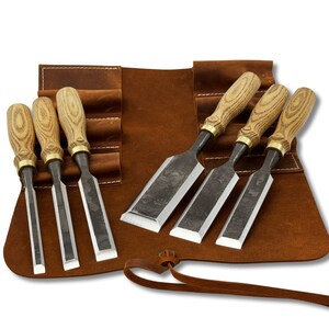 May include: A collection of wood chisels with wooden handles and metal blades, presented in a brown leather tool roll. The chisels are of varying sizes and are arranged to display their cutting edges. The tool roll is open, showcasing the chisels and their storage compartments.