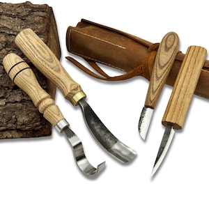 Puede incluir: Un juego de cuatro herramientas para tallar madera con mangos de madera y hojas de metal. Las herramientas están dispuestas con un estuche de cuero en el fondo. Los mangos tienen un patrón de veta de madera clara.