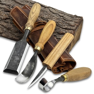 May include: A set of four wood carving tools with wooden handles and metal blades. The tools are displayed with a brown leather sheath and a piece of textured wood in the background. The handles have brass accents.