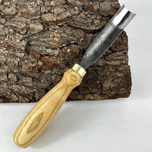 以下が含まれることがあります： 曲がった刃の木彫りガウジ。 刃は濃い色の金属でできており、真鍮のフェルールが付いた明るい色の木製のハンドルに取り付けられています。 ハンドルは丸みを帯びた人間工学に基づいた形状をしています。