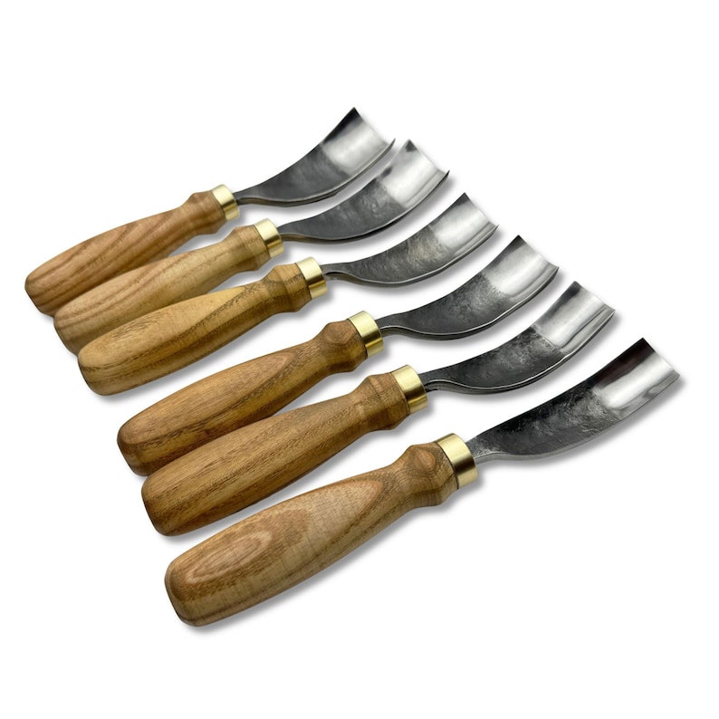 May include: A set of six wood carving gouges. Each tool has a curved, stainless steel blade and a light brown wooden handle with a brass ferrule. The tools are arranged diagonally on a white background.