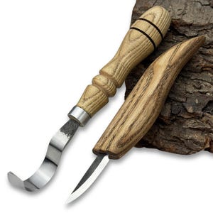 Puede incluir: Dos herramientas para tallar madera con mangos de madera y hojas de metal. Una herramienta tiene una hoja curva y la otra una hoja recta y puntiaguda. Los mangos son de color marrón claro con detalles en marrón oscuro.