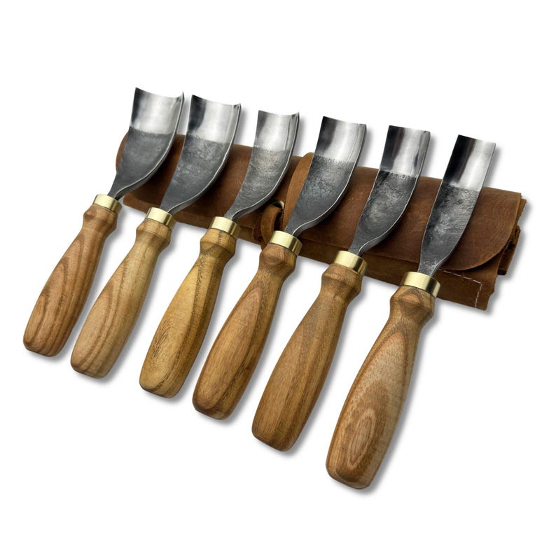 May include: A set of six wood carving gouges with curved steel blades and wooden handles. The tools are arranged in a brown leather tool roll. Each gouge has a brass ferrule where the blade meets the handle.