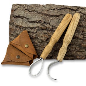 May include: Two wood-handled carving tools with curved blades and a small brown leather pouch with brass snap closures. The tools are set against a textured, dark brown bark background.