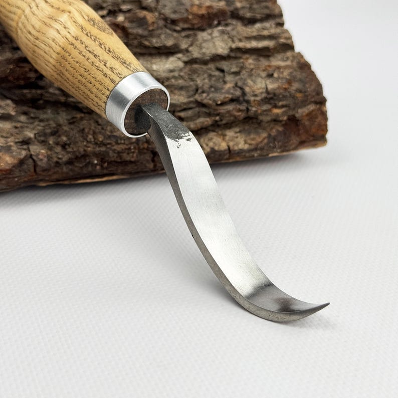 May include: A curved wood carving knife with a wooden handle and a metal ferrule. The blade is curved and has a sharp point.