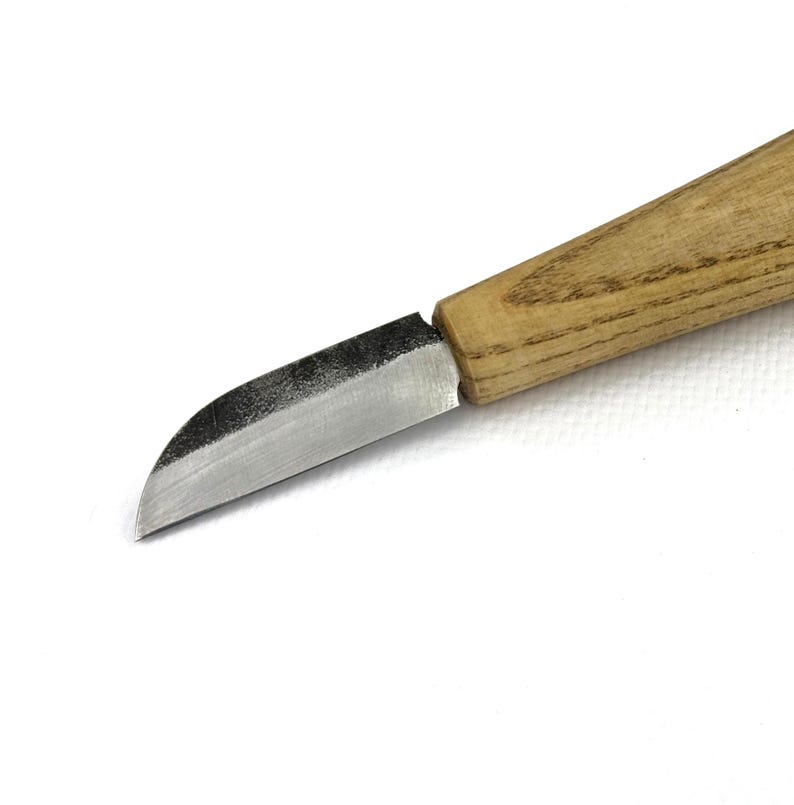 May include: A small, curved knife with a wooden handle. The blade is made of metal and has a slight curve to it. The handle is made of light brown wood and has a smooth finish.