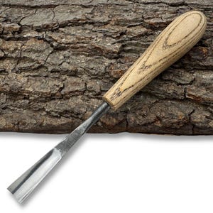 Puede incluir: Un formón para tallar madera con un mango de madera de color claro y una hoja plateada. El formón está en ángulo y parece afilado, diseñado para trabajos de carpintería detallados. El mango tiene un patrón de vetas de madera natural.