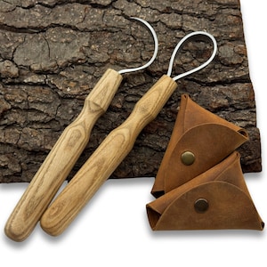 May include: Two wooden-handled tools with curved metal ends, possibly for crafting or sculpting, are displayed. They are accompanied by two small, brown leather pouches with snap closures. The tools and pouches rest on a textured, brown wooden surface.