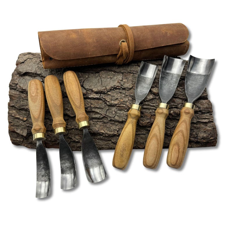 May include: A collection of six wood carving chisels with wooden handles and metal blades, alongside a brown leather tool roll. The tools are presented on a piece of textured bark.