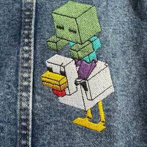 May include: A green Minecraft zombie riding a white chicken on a blue denim background.