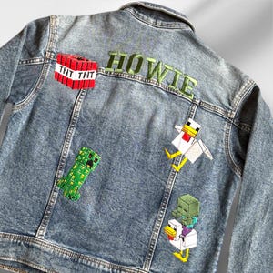 May include: A blue denim jacket with embroidered patches. The patches include a green creeper, a white chicken, a zombie holding a chicken, and a red block with the text "TNT TNT". The text "HOWIE" is embroidered in green on the back of the jacket.