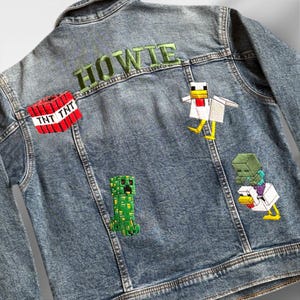 May include: A blue denim jacket with embroidered patches featuring Minecraft characters, including a creeper, a chicken, and a zombie holding a chicken. The name "HOWIE" is embroidered in green on the back of the jacket.