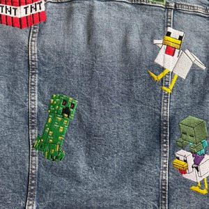 May include: A blue denim jacket with embroidered patches featuring Minecraft characters, including a creeper, a chicken, and a TNT block. The name "HOWIE" is embroidered in green on the back of the jacket.