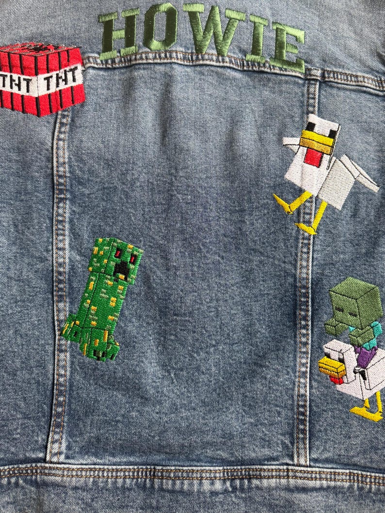 May include: A blue denim jacket with embroidered patches featuring Minecraft characters, including a creeper, a chicken, and a TNT block. The name "HOWIE" is embroidered in green on the back of the jacket.